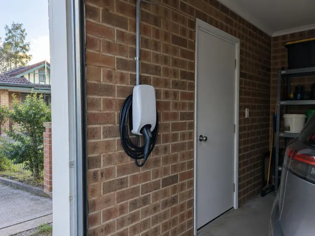 Wall-mounted EV charger on a brick garage wall beside a white door and parked car in Mayfield