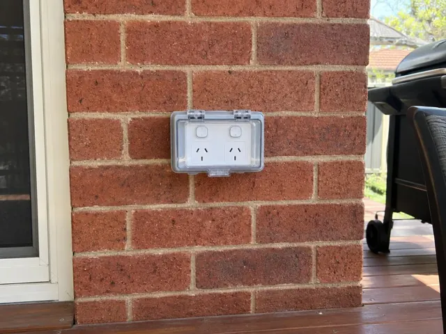 Weatherproof double power point on a red brick exterior wall beside a deck in Waratah